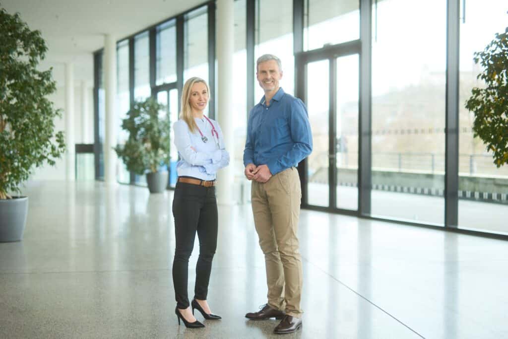 Leasymed 7 Arzt und Ärztin stehen nebeneinander in modernem Glas Gebäude