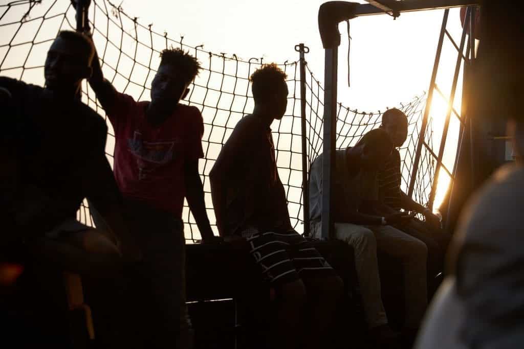 Sonnenuntergang auf dem Mittelmeer und dem Seenotrettungsschiff der NGO Sea Eye mit Silhouetten von Männern an Deck